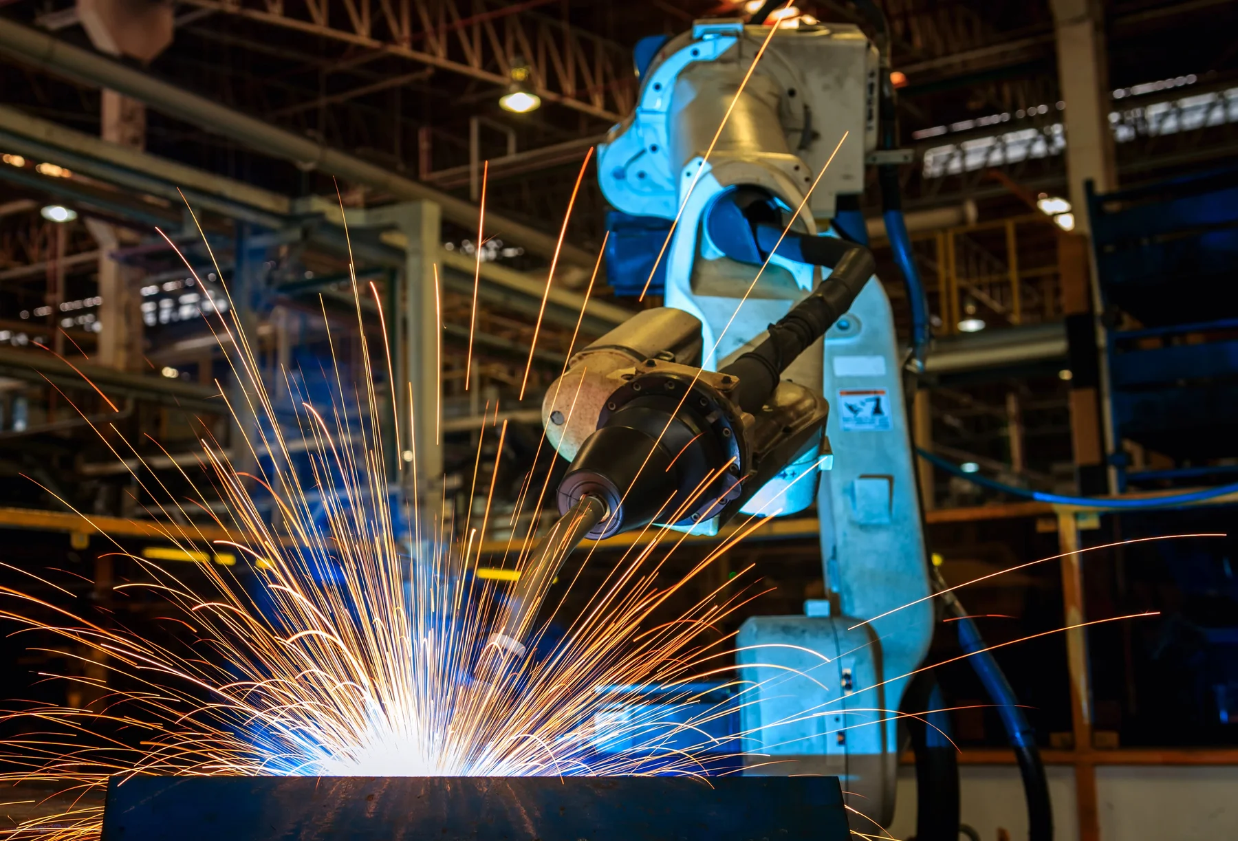 Blauer Industriearm beim Schweißen eines Bauteils in einer Produktionshalle