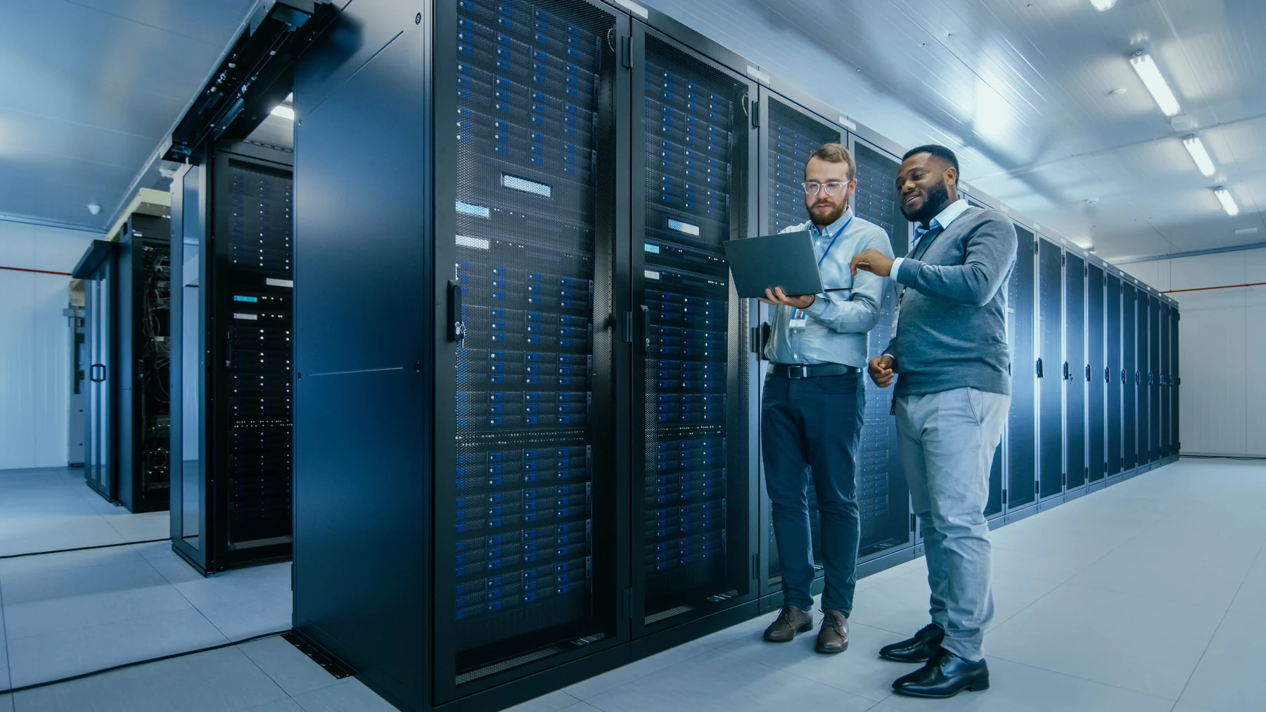 Zwei IT-Fachkräfte besprechen Arbeiten an einem Laptop zwischen Serverracks im Rechenzentrum