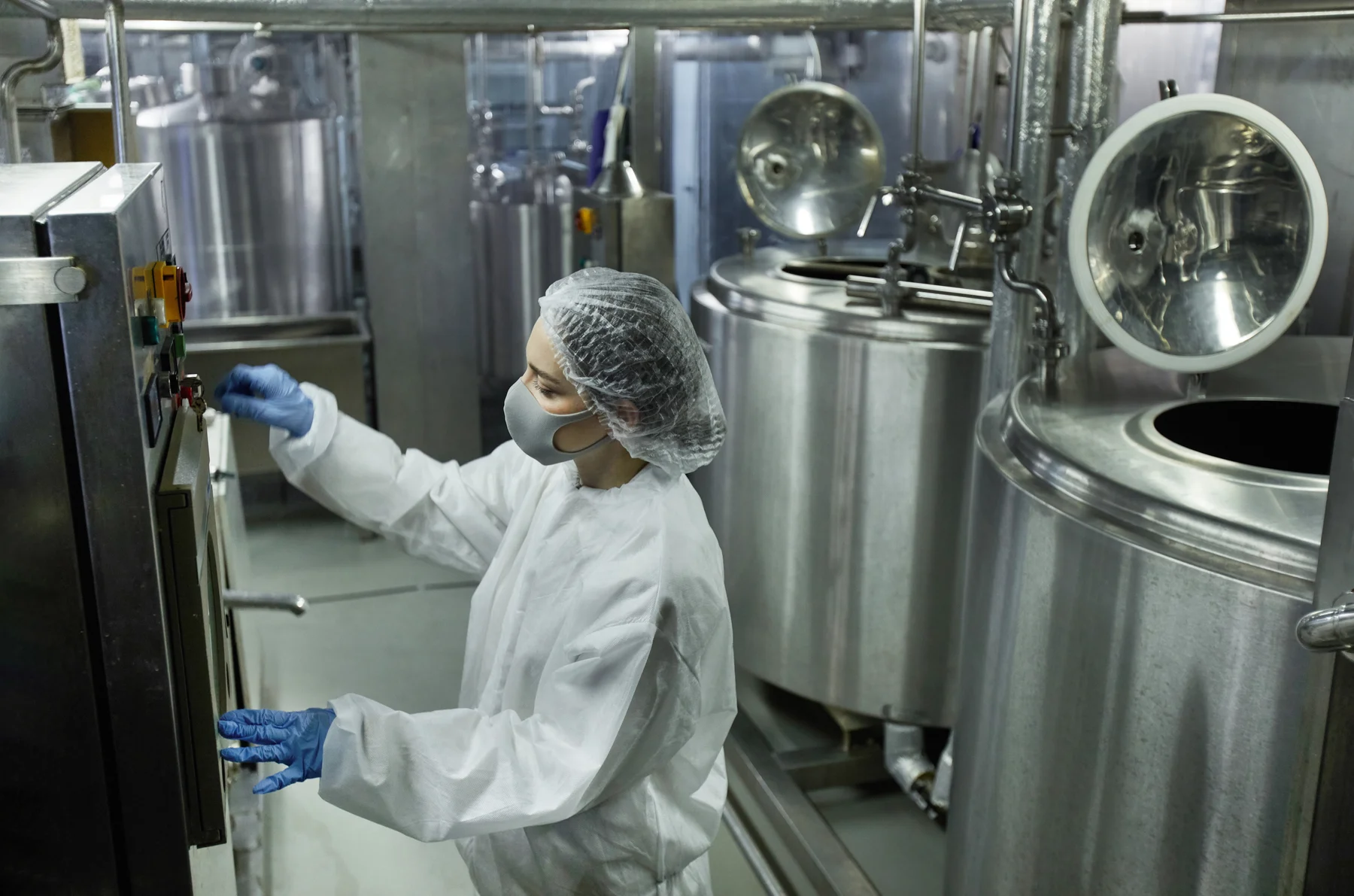 Mitarbeiterin bedient eine Anlage zwischen großen Prozessbehältern einer Lebensmittelfabrik